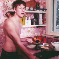 Album cover of a man cooking in a floral-wallpapered kitchen